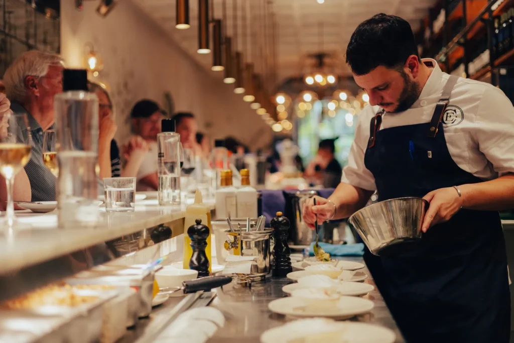 Chef plating a dish at the counter as guests look on at El Camino Restaurant
