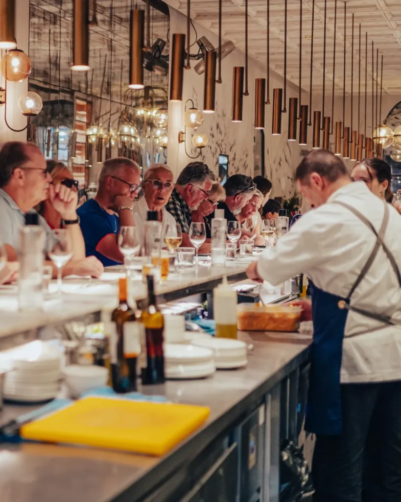 Guests seated along the counter watching a chef prepare food at El Camino Restaurant