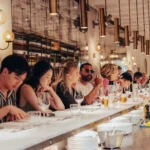 Guests with beers and wine seated along the marble counter under an antiqued mirror at El Camino Restaurant