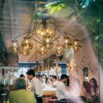 Busy dining room beneath a brass globe chandelier with waiters and guests at El Camino Restaurant