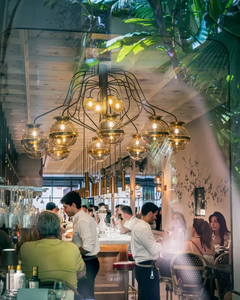 Busy dining room beneath a brass globe chandelier with waiters and guests at El Camino Restaurant