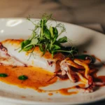 Grilled squid in a paprika sauce with herb oil and pea shoots at El Camino Restaurant