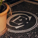 Black-and-white mosaic floor with the El Camino monogram beside a terracotta planter at El Camino Restaurant