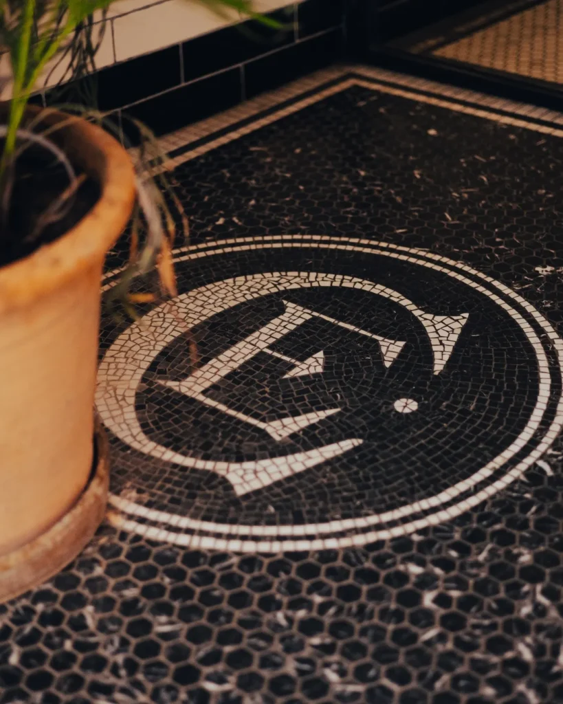 Black-and-white mosaic floor with the El Camino monogram beside a terracotta planter at El Camino Restaurant