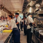 Kitchen brigade at work along the open pass beneath brass pendant lights at El Camino Restaurant