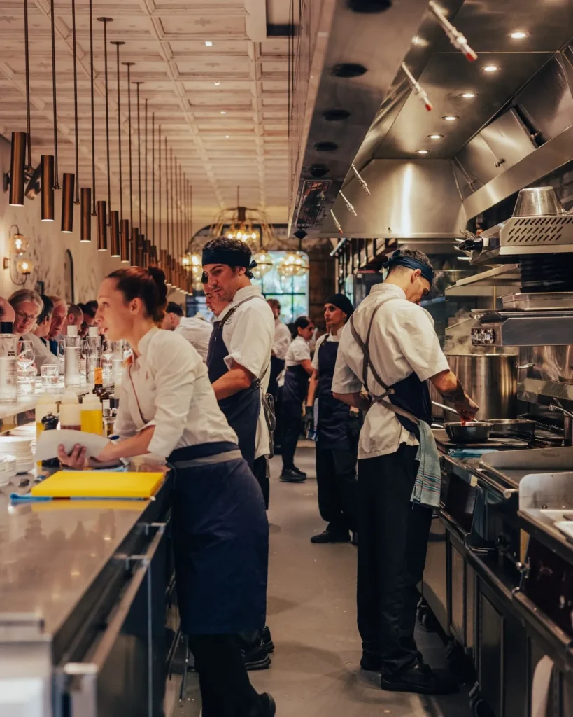 Kitchen brigade at work along the open pass beneath brass pendant lights at El Camino Restaurant