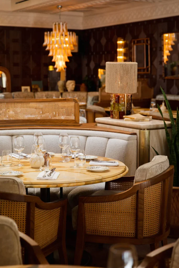 Curved banquette and cane chairs around a marble table beneath a rattan lamp at Gigi Rigolatto Paris