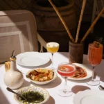 Cocktails, charcuterie and dips with grissini on a sunlit table at Gigi Rigolatto Paris