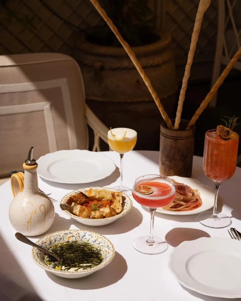 Cocktails, charcuterie and dips with grissini on a sunlit table at Gigi Rigolatto Paris