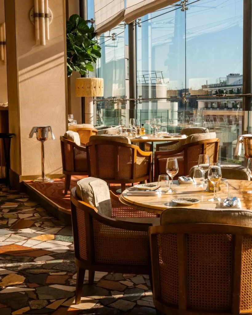Cane armchairs and marble tables by the windows over a terrazzo floor at Gigi Rigolatto Paris