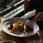Seared fish over green sauce with grilled aubergine being cut into by a guest at Gigi Rigolatto Paris