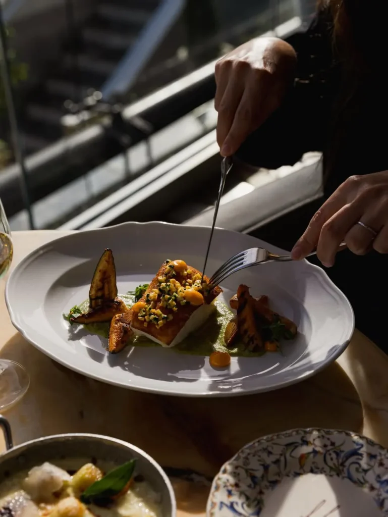 Seared fish over green sauce with grilled aubergine being cut into by a guest at Gigi Rigolatto Paris