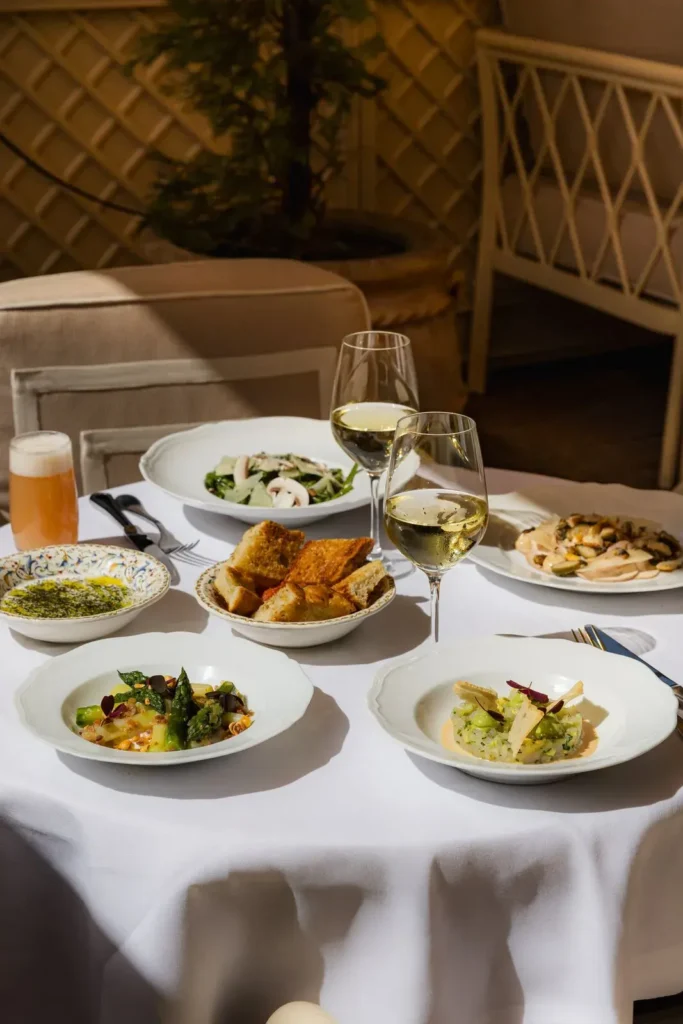 Spread of salad, risotto, bread and white wine on a white-clothed table at Gigi Rigolatto Paris