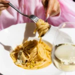 Creamy pistachio pasta twirled on a fork over a plate with white wine at Gigi Rigolatto Paris