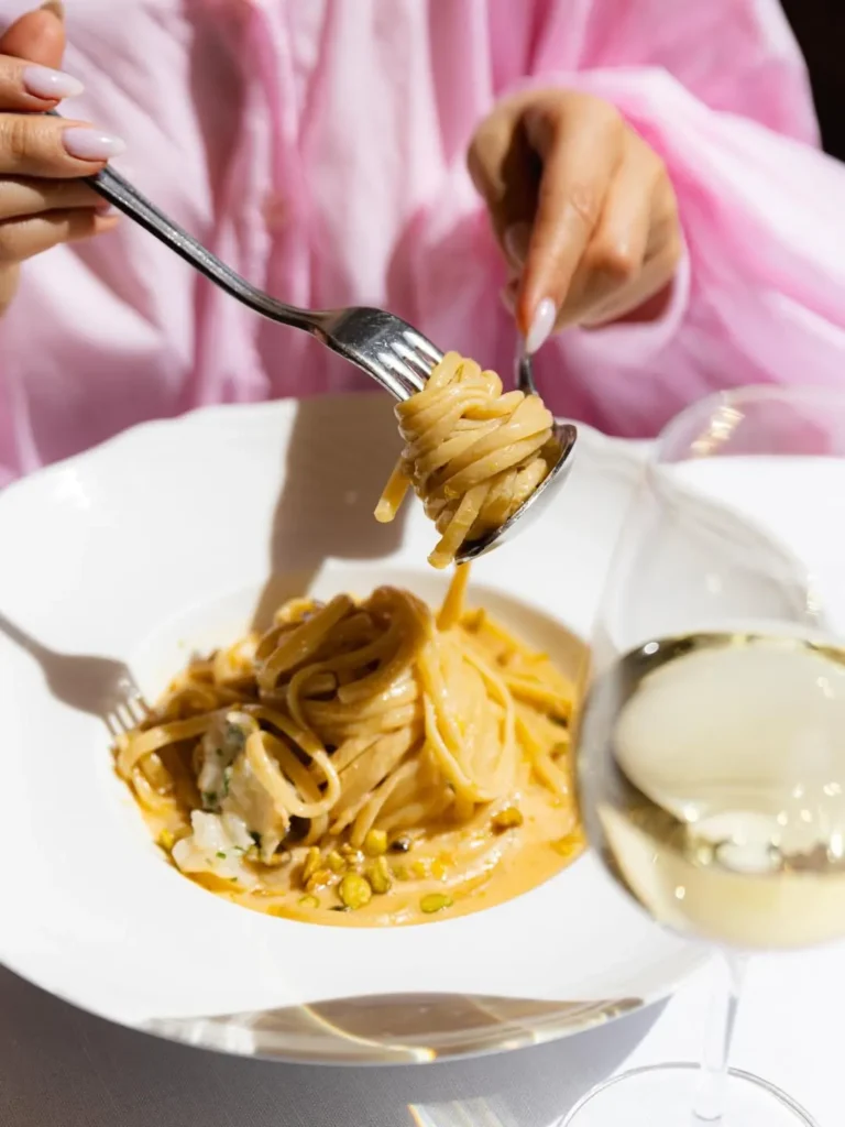 Creamy pistachio pasta twirled on a fork over a plate with white wine at Gigi Rigolatto Paris