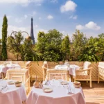 Terrace tables under a striped awning with the Eiffel Tower beyond the greenery at Gigi Rigolatto Paris