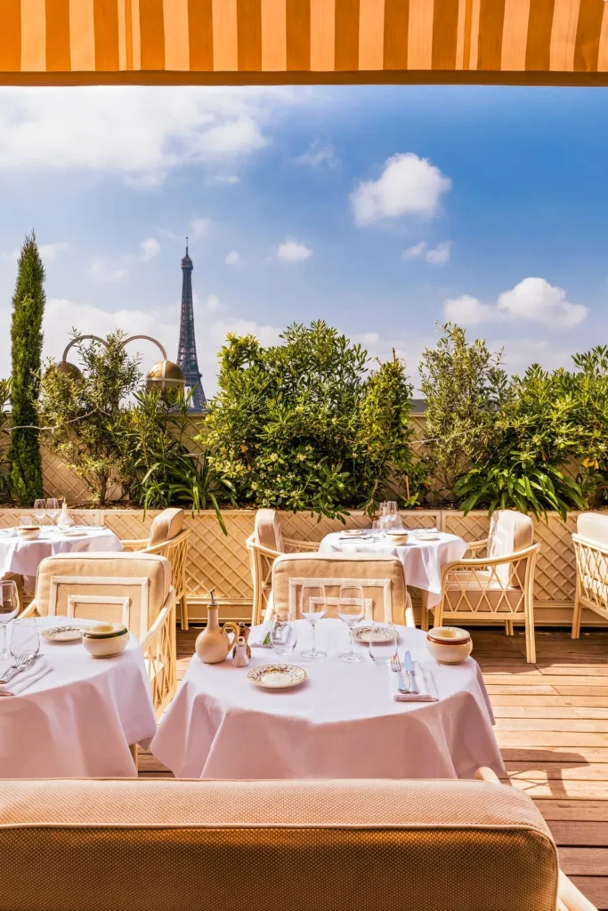 Terrace tables under a striped awning with the Eiffel Tower beyond the greenery at Gigi Rigolatto Paris
