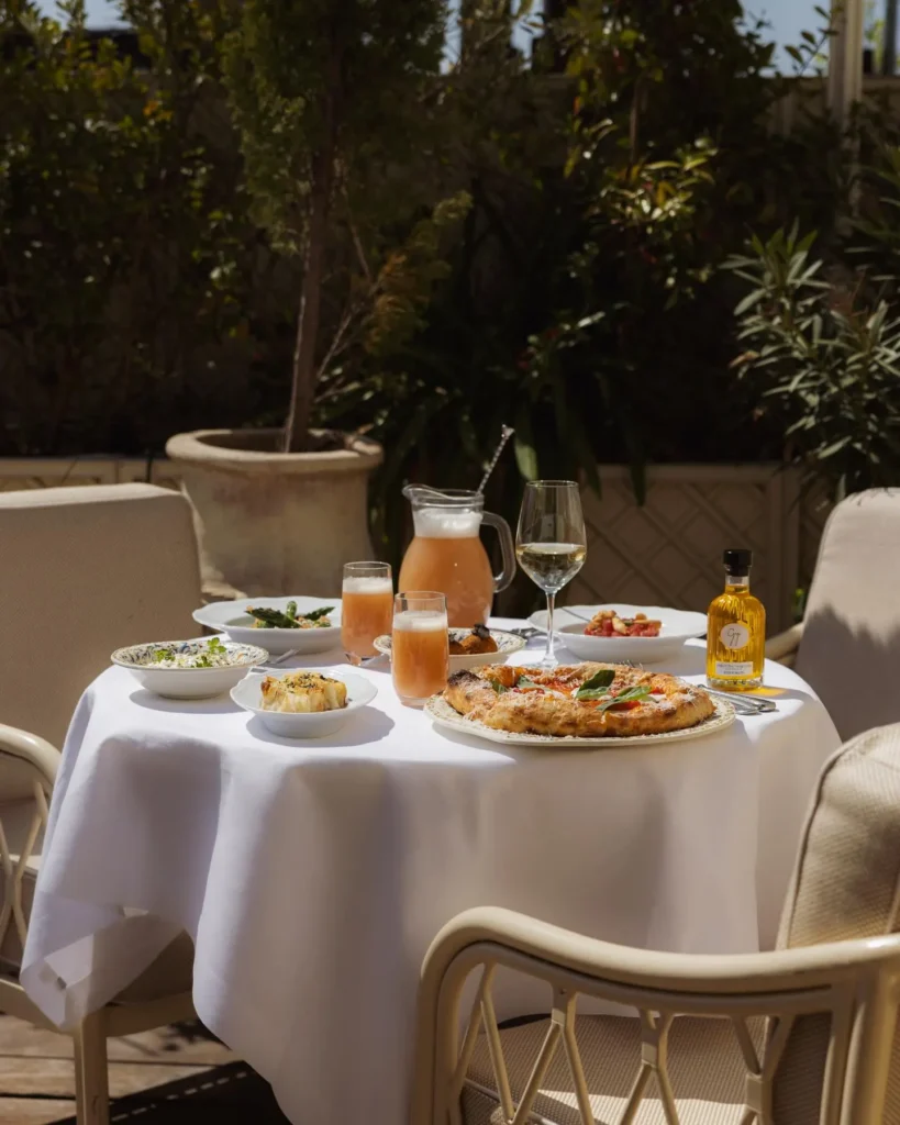 Pizza, sides and pink drinks on a terrace table in the sun at Gigi Rigolatto Paris