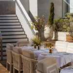 Cushioned terrace chairs and white-clothed tables beside a staircase and planters at Gigi Rigolatto Paris