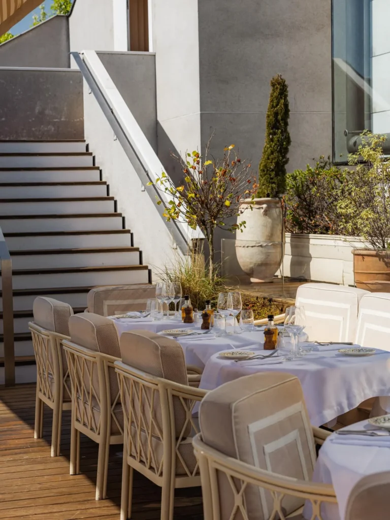 Cushioned terrace chairs and white-clothed tables beside a staircase and planters at Gigi Rigolatto Paris