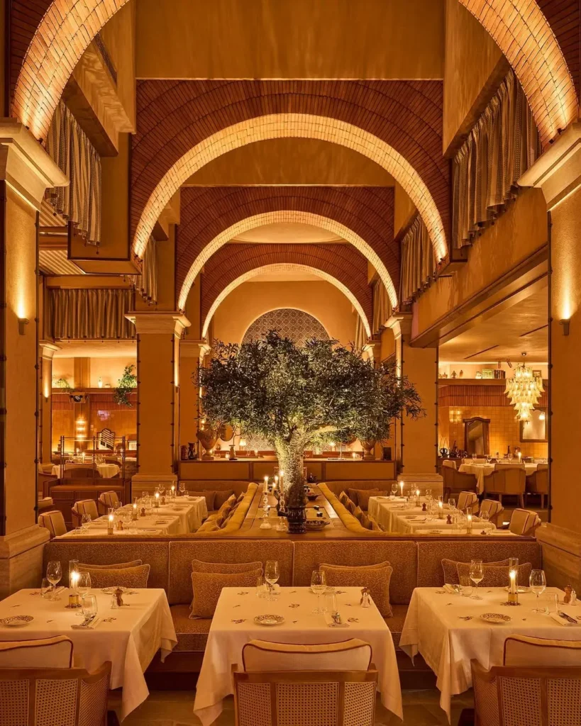 Vaulted brick-arched dining hall with a central olive tree and white-clothed tables at Gigi Rigolatto Paris