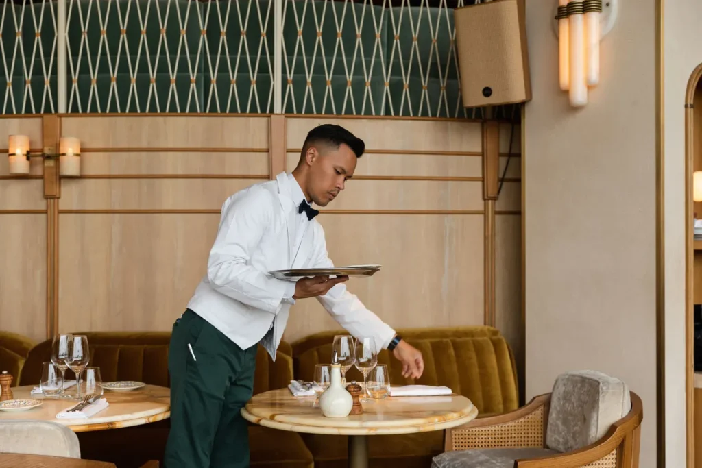 Waiter in a bow tie setting a marble table with a tray at Gigi Rigolatto Paris