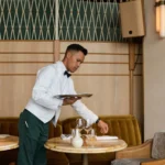 Waiter in a bow tie setting a marble table with a tray at Gigi Rigolatto Paris