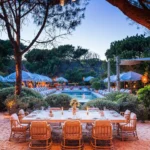 Long dining table on the sand overlooking the lit pool at dusk at Gigi Rigolatto Saint-Tropez