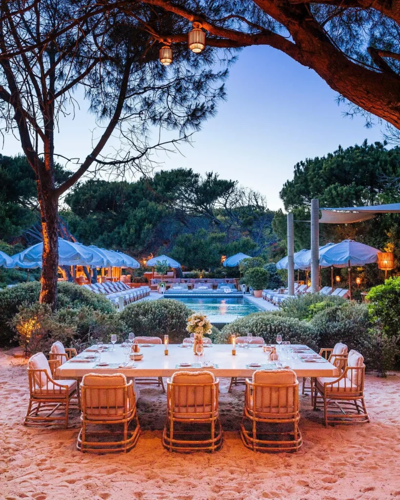 Long dining table on the sand overlooking the lit pool at dusk at Gigi Rigolatto Saint-Tropez