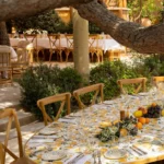 Oval table dressed in a lemon-print cloth with fruit and flowers under a pine at Gigi Rigolatto Saint-Tropez