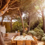 Long table set beside an outdoor bar among umbrella pines at Gigi Rigolatto Saint-Tropez