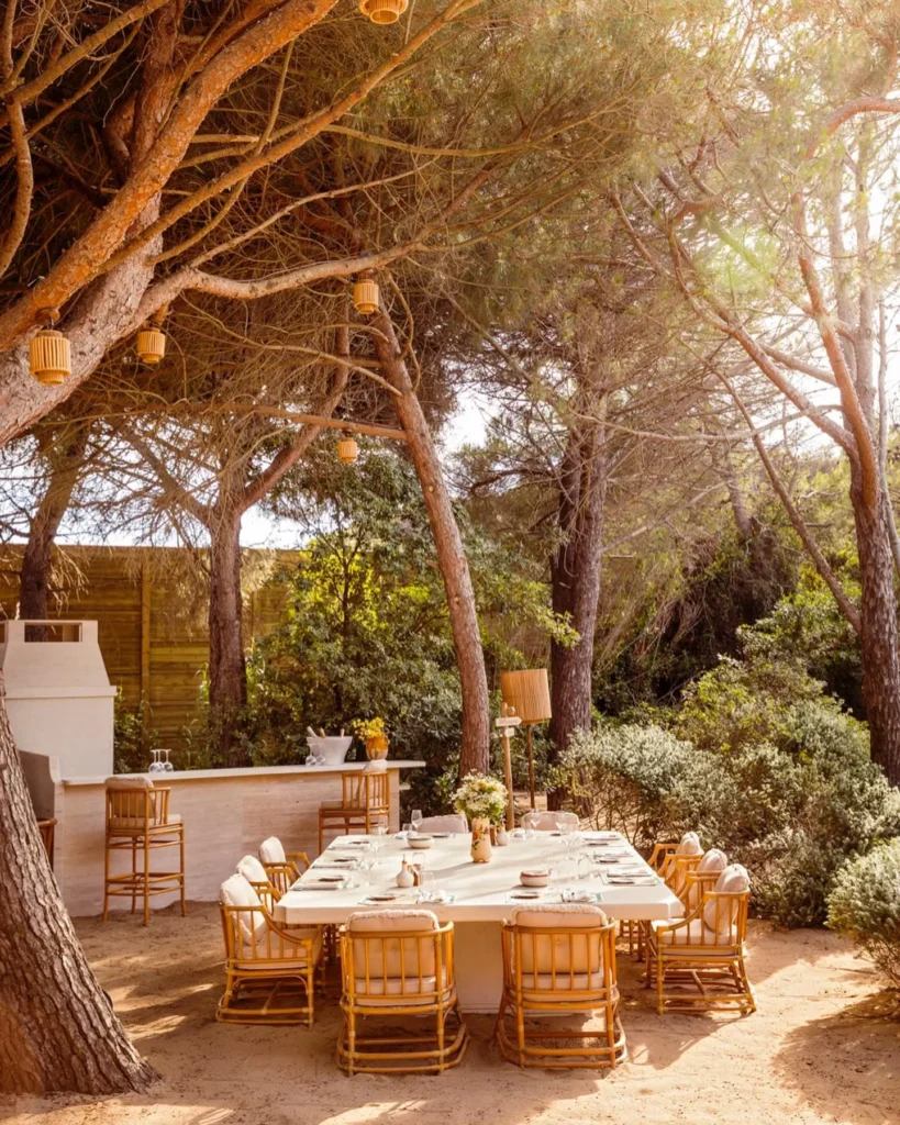 Long table set beside an outdoor bar among umbrella pines at Gigi Rigolatto Saint-Tropez