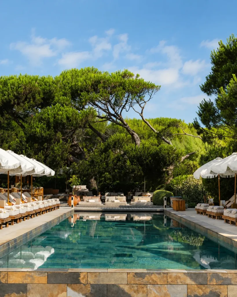 Swimming pool flanked by fringed umbrellas and sunbeds beneath umbrella pines at Gigi Rigolatto Saint-Tropez