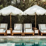 Striped loungers beneath fringed parasols against greenery at the pool at Gigi Rigolatto Saint-Tropez