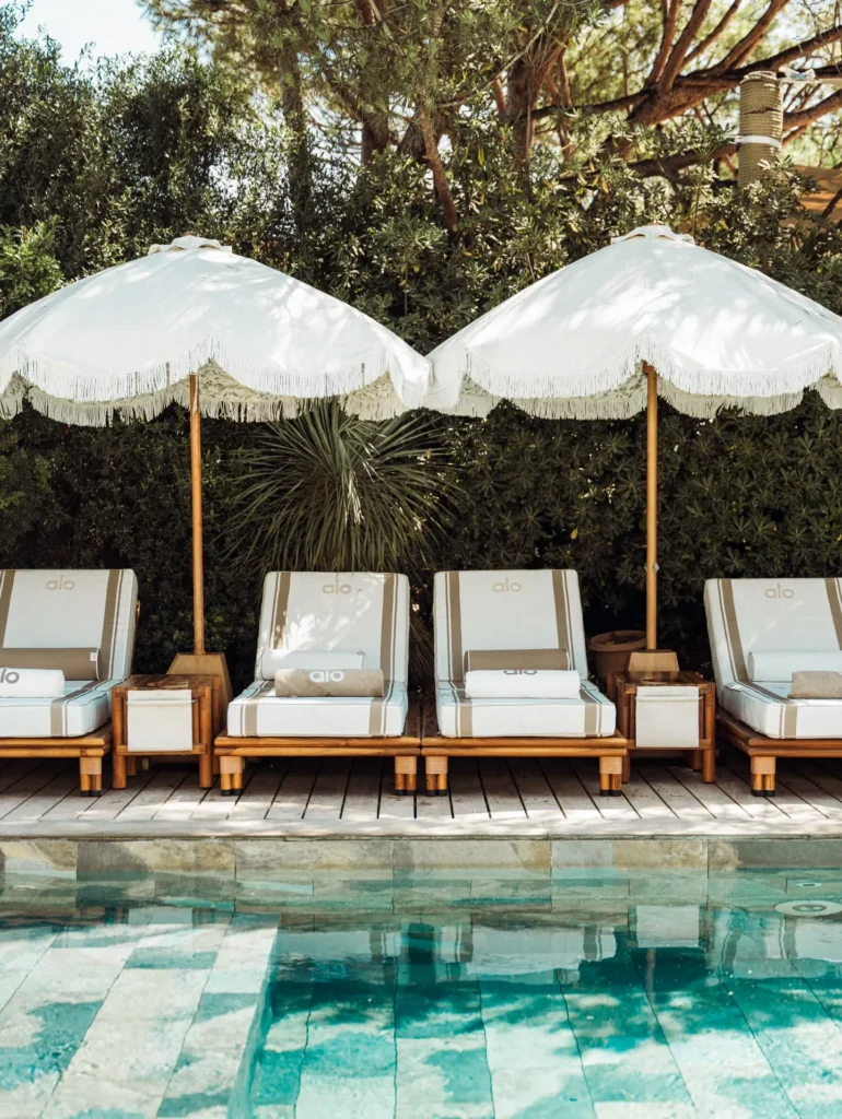 Striped loungers beneath fringed parasols against greenery at the pool at Gigi Rigolatto Saint-Tropez