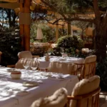 Dappled dining tables with shearling-trimmed rattan chairs among greenery at Gigi Rigolatto Saint-Tropez