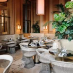 Cream banquette and wire chairs around marble-topped tables with lush plants at Girafe Paris