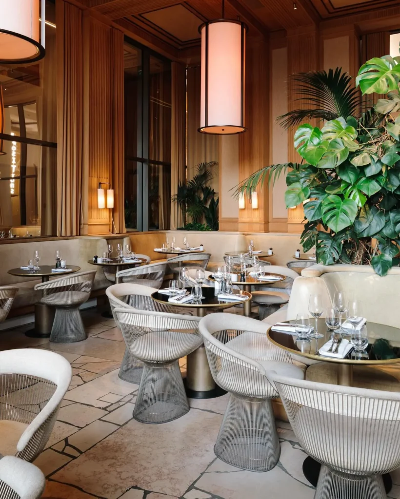 Cream banquette and wire chairs around marble-topped tables with lush plants at Girafe Paris