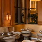 Suede banquette and wire chairs under warm sconce lighting and curtains at Girafe Paris