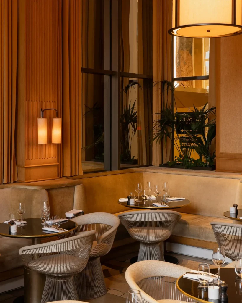 Suede banquette and wire chairs under warm sconce lighting and curtains at Girafe Paris
