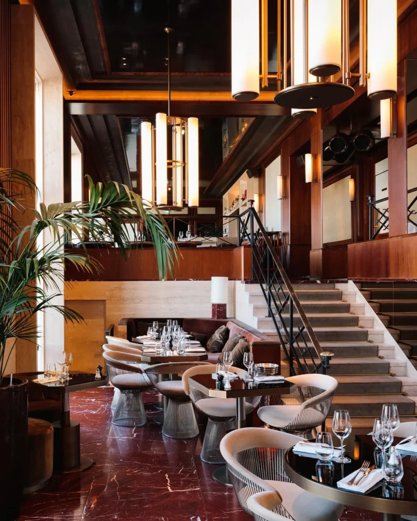 Art Deco dining room with red marble floor, wire chairs and a carpeted staircase at Girafe Paris