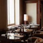 Set tables with velvet armchairs beside a tall window and marble lamp at Girafe Paris