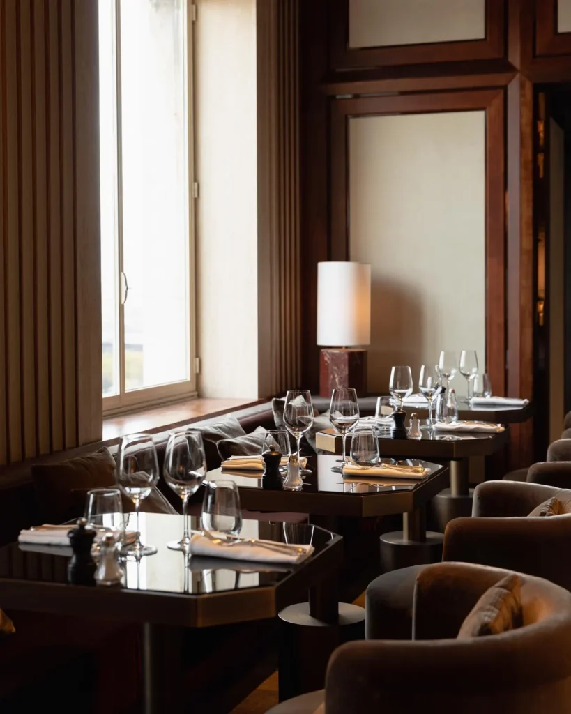 Set tables with velvet armchairs beside a tall window and marble lamp at Girafe Paris