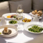 Spread of fish on lentils, octopus, greens and bread with white wine on a terrace table at Girafe Paris