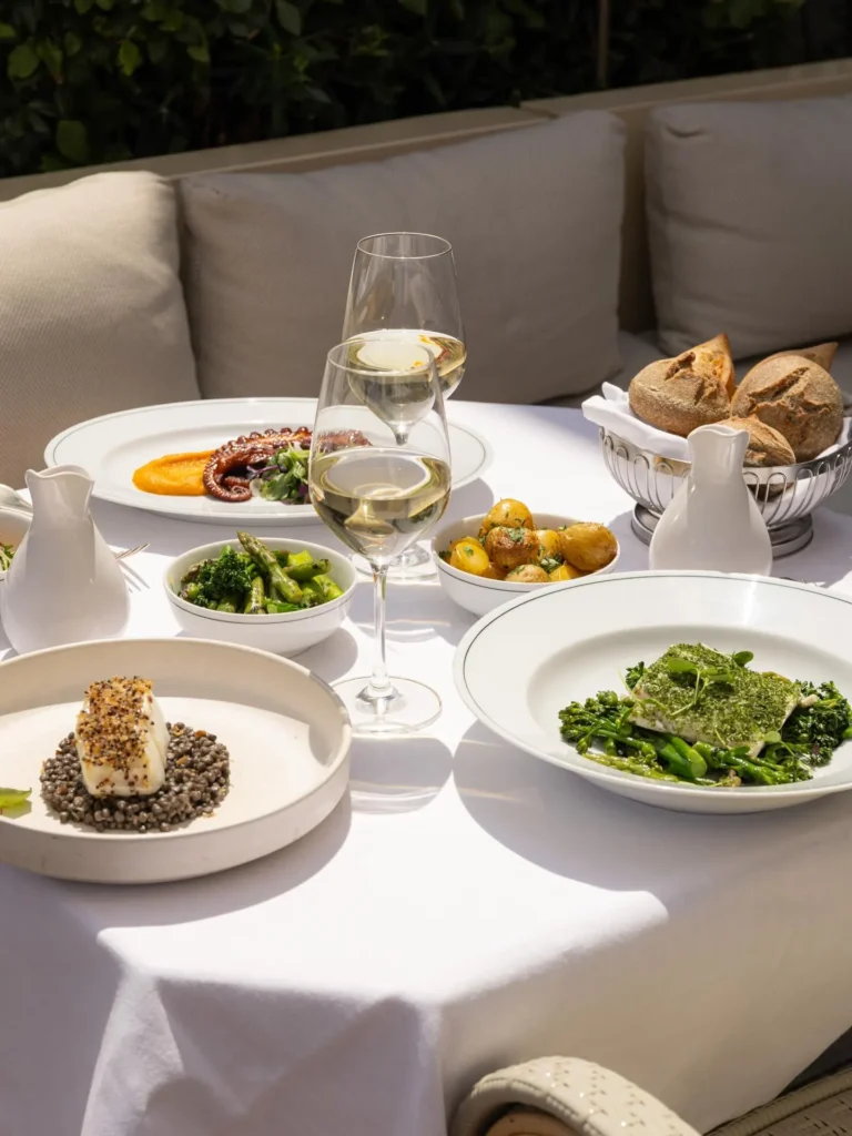 Spread of fish on lentils, octopus, greens and bread with white wine on a terrace table at Girafe Paris