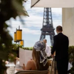 Guest in a printed headscarf reading the menu with the Eiffel Tower beyond at Girafe Paris