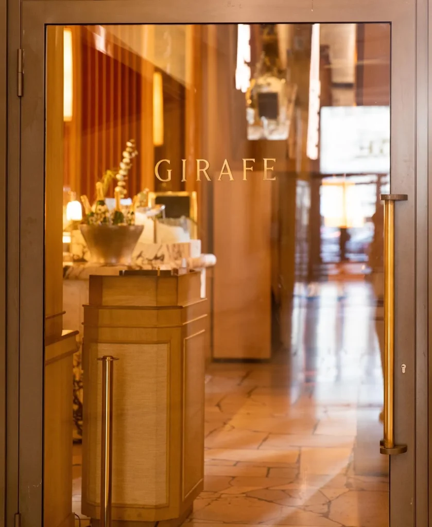 Gold GIRAFE lettering etched on a glass door looking into the wood-panelled interior at Girafe Paris