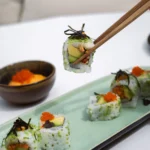 Avocado sushi rolls topped with roe and nori lifted by chopsticks at Girafe Paris