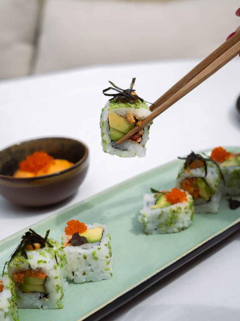 Avocado sushi rolls topped with roe and nori lifted by chopsticks at Girafe Paris