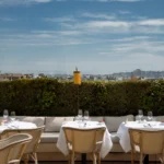 Terrace banquette and rattan chairs above a hedge with the Paris skyline at Girafe Paris